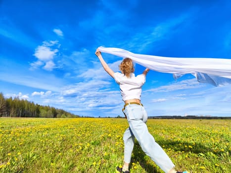 A joyful individual races across a blooming yellow flower field, waving a white scarf as they embrace the warmth of a beautiful day.