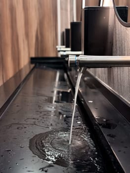 Modern public restroom faucet with water flow on black basin surface.