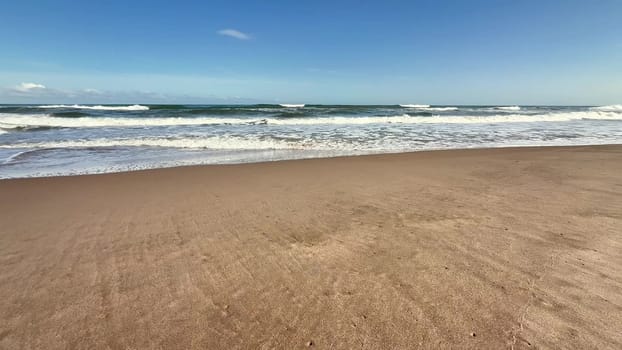A serene beach scene showcasing soft, warm sand, gentle ocean waves, and a bright, vibrant blue sky above