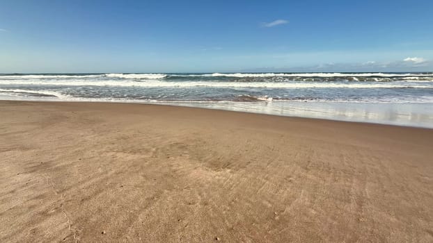 A serene beach scene with gentle waves lapping the shore beneath a bright blue sky and fluffy cotton clouds