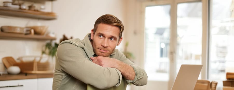 Vertical portrait of handsome masculine man, sitting on chair, looking aside, waiting for an order in coffee shop.
