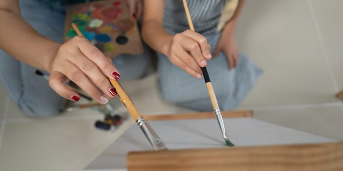 A close-up shot of mother and daughter painting together, emphasizing their hands working together in creativity.