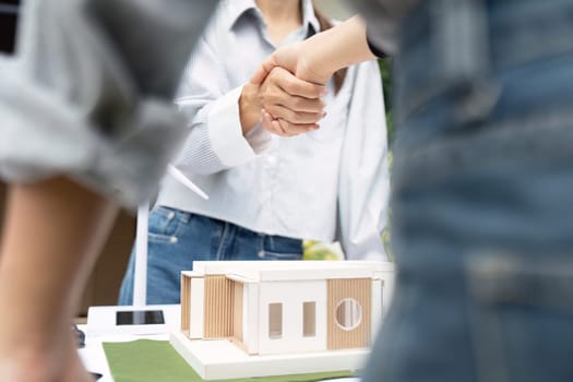 Two sustainability-focused engineers celebrating their successful collaboration on an architectural project with a model house outdoors.