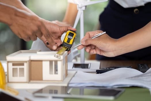 Engineers measuring a model house for sustainable construction, showcasing teamwork and innovative design planning.
