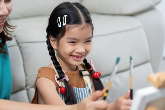 A young girl beams with joy as she paints with her mother, sharing a delightful and creative experience together.