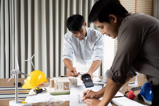 Engineers focusing on creating innovative sustainable designs while working on blueprints and models at a collaborative workspace.
