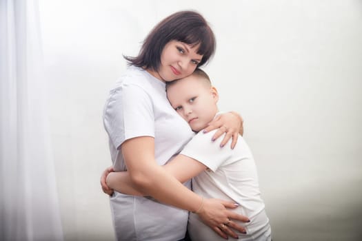 A mother and her son are hugging gently in a softly lit room, expressing affection and connection in a tender moment of love.