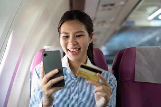 A cheerful business traveler smiles while using her phone and a credit card for a transaction during the flight.