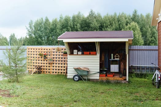 A rustic storage shed stands within a backyard adorned with a wheelbarrow overflowing with wood, a decorative wooden lattice, and potted plants, ideal for illustrating rural life