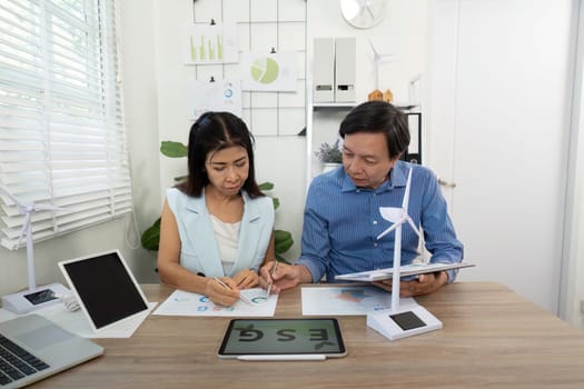 A woman and man analyzing charts on ESG performance during a meeting in their office, highlighting sustainability metrics and strategies.