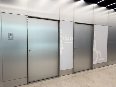 Modern public restroom entrance with minimalist metallic doors and universal accessibility signs. Clean design, symbols for baby changing station and wheelchair accessible restroom