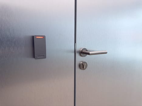 Close up of metal door with handle and electronic card reader. Concept of restricted access, modern security systems, staff area control and building access technology
