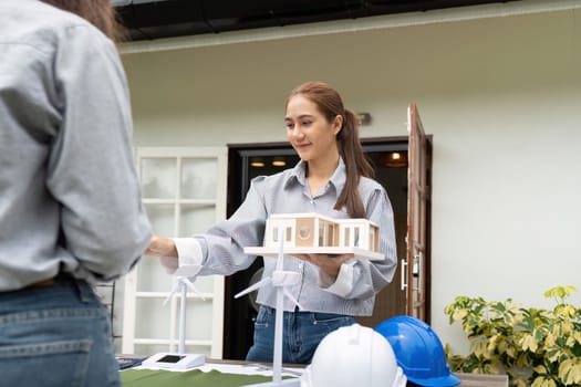 A sustainability engineer presenting eco-friendly building models and renewable resources to a client in an outdoor setting, emphasizing collaboration and innovation.