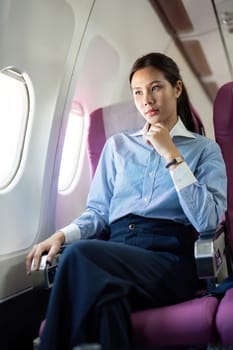 A thoughtful businesswoman seated in an airplane, gazing out the window and contemplating her journey ahead during business travel.