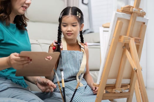 A mother guides her daughter in a creative painting session, sharing tips and encouragement in their bright living room.