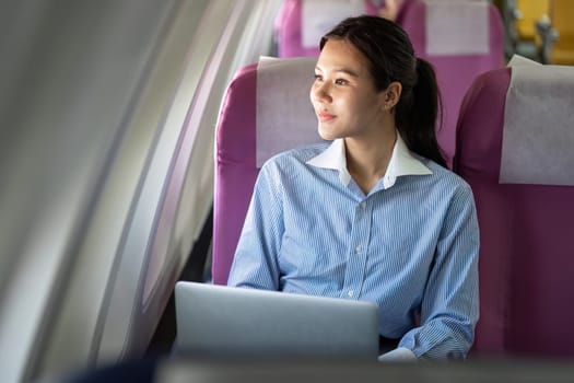 A young professional woman smiles while using her laptop on an airplane, showcasing the convenience of business travel.