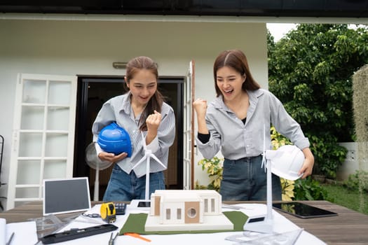 Two sustainability engineers joyfully celebrate the success of their architectural project while displaying the model outdoors.