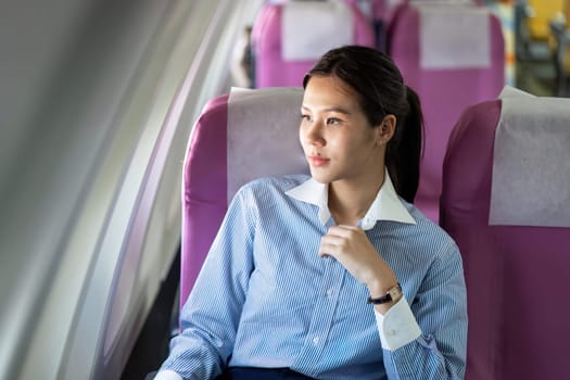 A young woman dressed in formal attire gazes thoughtfully out the airplane window during her business travel, calmly enjoying her journey.