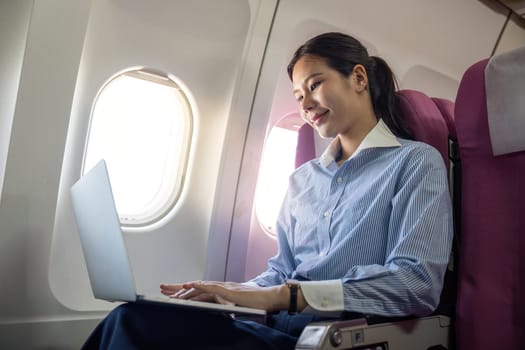 A business traveler works on her laptop while seated onboard the aircraft, focusing on productivity during her flight.
