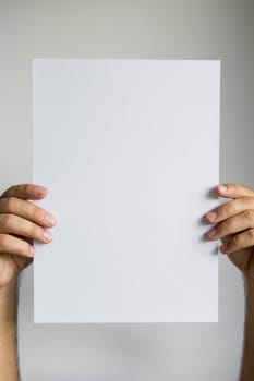 Hands holding blank white paper against plain background.