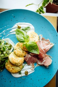 Plate of Crispy Herb Fritters with Prosciutto and Basil Garnish on a Vibrant Blue Dish