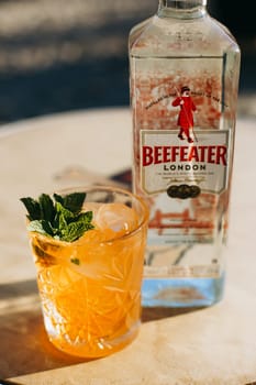 Refreshing Cocktail with Orange and Mint Served in a Glass Next to a Bottle of London Gin