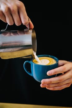 Skilled Barista Pouring Cream Into Blue Coffee Cup with Latte Art in a Cozy Cafe Setting