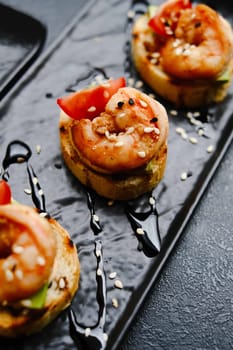 Savory Shrimp Appetizer on Toasted Bread with Tomato Garnish and Balsamic Drizzle on Black Plate