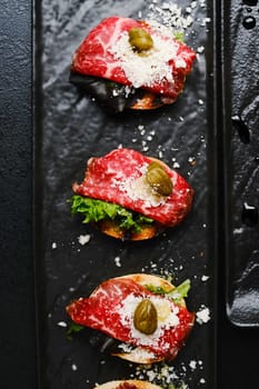 Gourmet Meat Slices with Capers and Cheese on a Black Plate Styled for Elegant Presentation