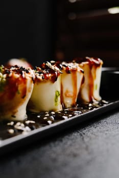Gourmet Sushi Rolls Artistically Plated on a Black Slate with Garnishes and Sauce