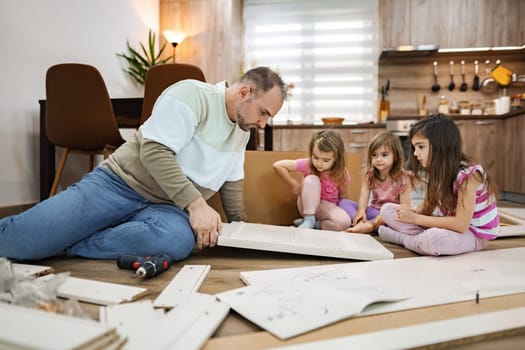 A father works with his three young daughters on assembling furniture. The cozy living room is filled with scattered parts, as laughter and collaboration fill the air in this weekend bonding activity.