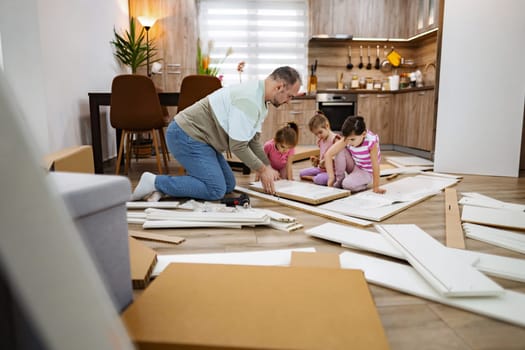 Grandfather engages with his grandchildren as they assemble furniture in a warmly lit living room. Cardboard boxes and tools surround them, highlighting their teamwork and shared joy.
