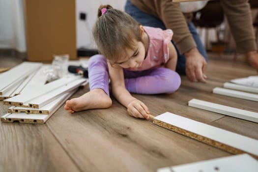 In a warm and inviting living space, a child observes closely as an adult works on assembling wooden pieces. The focus on their task showcases their bond and the joy of learning together.