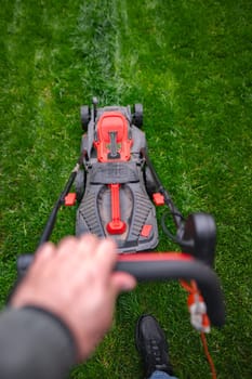 A hand grips the mower handle, slicing through lush grass in a neatly maintained garden. The sun casts a warm glow, highlighting the fresh cut lines in the verdant landscape.