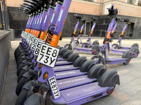 Moscow, Russia, April 24, 2025: Close up of branded electric scooters lined up for rent on city sidewalk, emphasizing license plates and urban micro mobility solutions in public spaces