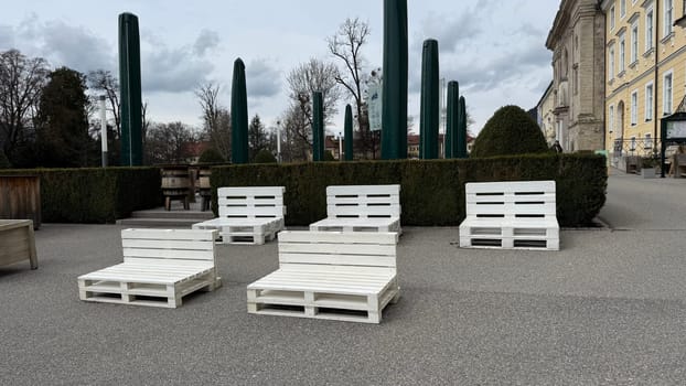 Tegernsee, Germany - March 30, 2025: Outdoor seating area features white pallet furniture in a park for relaxation near lake Tegernsee and church Pfarrkirche St. Quirinus