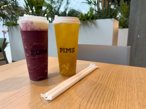 Moscow, Russia, April 25, 2025: Two takeaway drinks from PIMS cafe with paper straws on wooden table. Modern tea bar concept highlighting clean presentation and eco friendly details