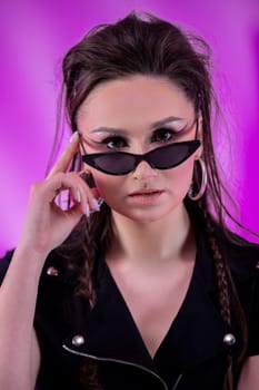 A stylish woman poses confidently in trendy sunglasses, showcasing her modern style against a colorful backdrop