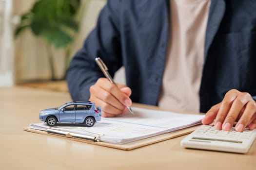 Hands writing a signature on car lease documents while calculating taxes. Financial agreements for loans, contracts, and transactions in buying or selling vehicles.