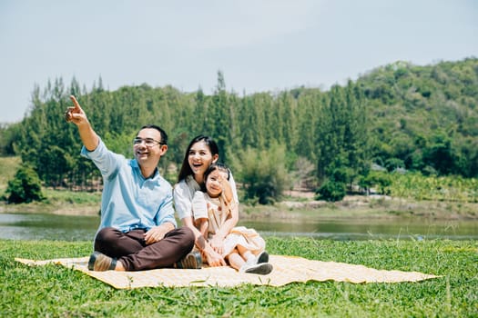 Asian family father mother and daughter sitting on blanket spring meadow field grass sunny day in park cheerful sweet kid girl, parents and child picnic enjoying outdoors together, Family relaxation
