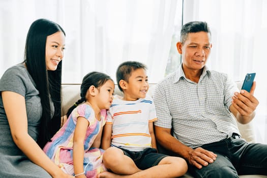 Parents and kids enjoy entertainment on a smartphone laughing together on a couch. The image illustrates familial happiness bonding and shared technology experiences at home.