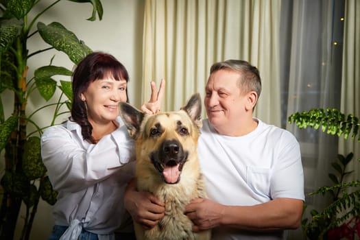 A middle-aged couple joyfully interacts with their german shepherd dog inside their home, showcasing their love and bond with family.