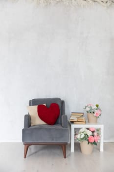 An armchair with cushions and a table with books and flowers in the interior of a white room