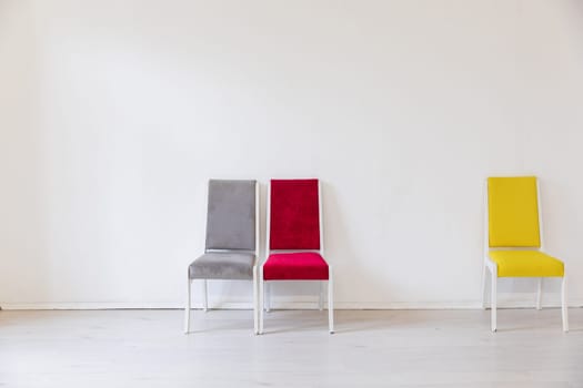 Three chairs of different colors in the interior of a white room