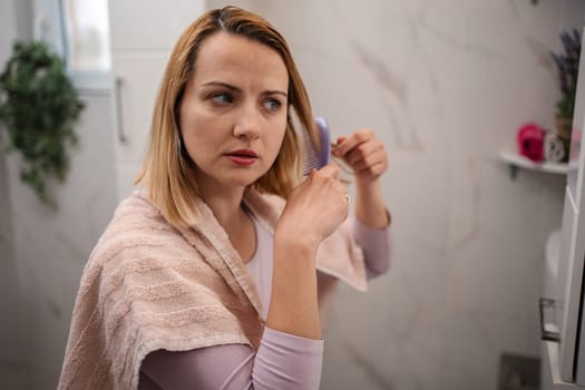 Mid adult woman combing her hair in the bathroom after a shower, looking at the mirror