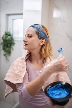 Young woman applying blue dye to her hair, doing a hair coloring treatment at home