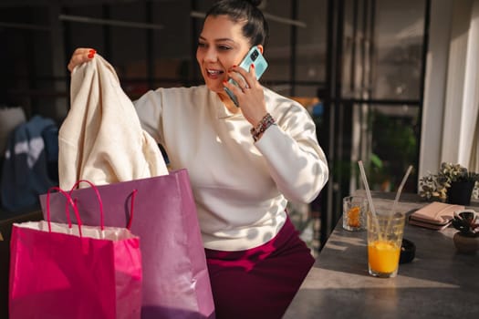 A woman enjoys shopping while chatting on the phone at a cafe.