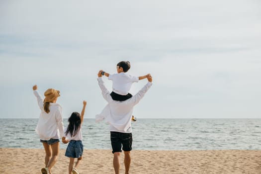 A blissful family moment on the beach at sunset. The father carries his son on shoulders surrounded by raised arms capturing the happiness and relaxation of a perfect summer vacation.