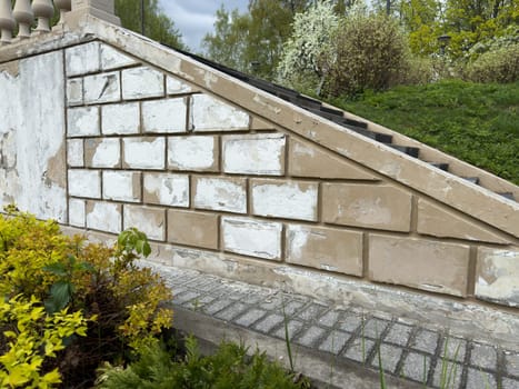 Detail view of chipped plaster and partially repainted brick wall along a public park stairway balustrade, showing visible restoration process and maintenance of urban park infrastructure