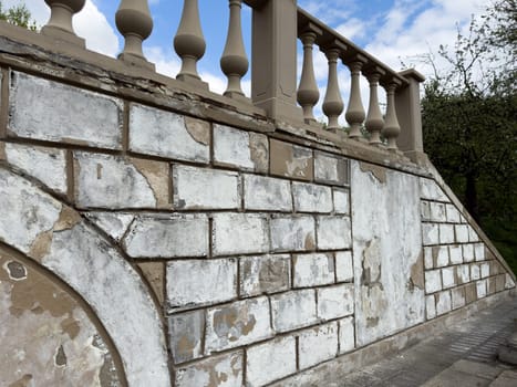 Old balustrade and staircase wall with flaking paint and damaged surface captured during restoration process in landscaped park area, showing architectural details and signs of ongoing renewal work